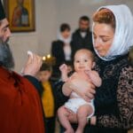 Chrzest dziecka w kościele, matka trzyma niemowlę obok księdza