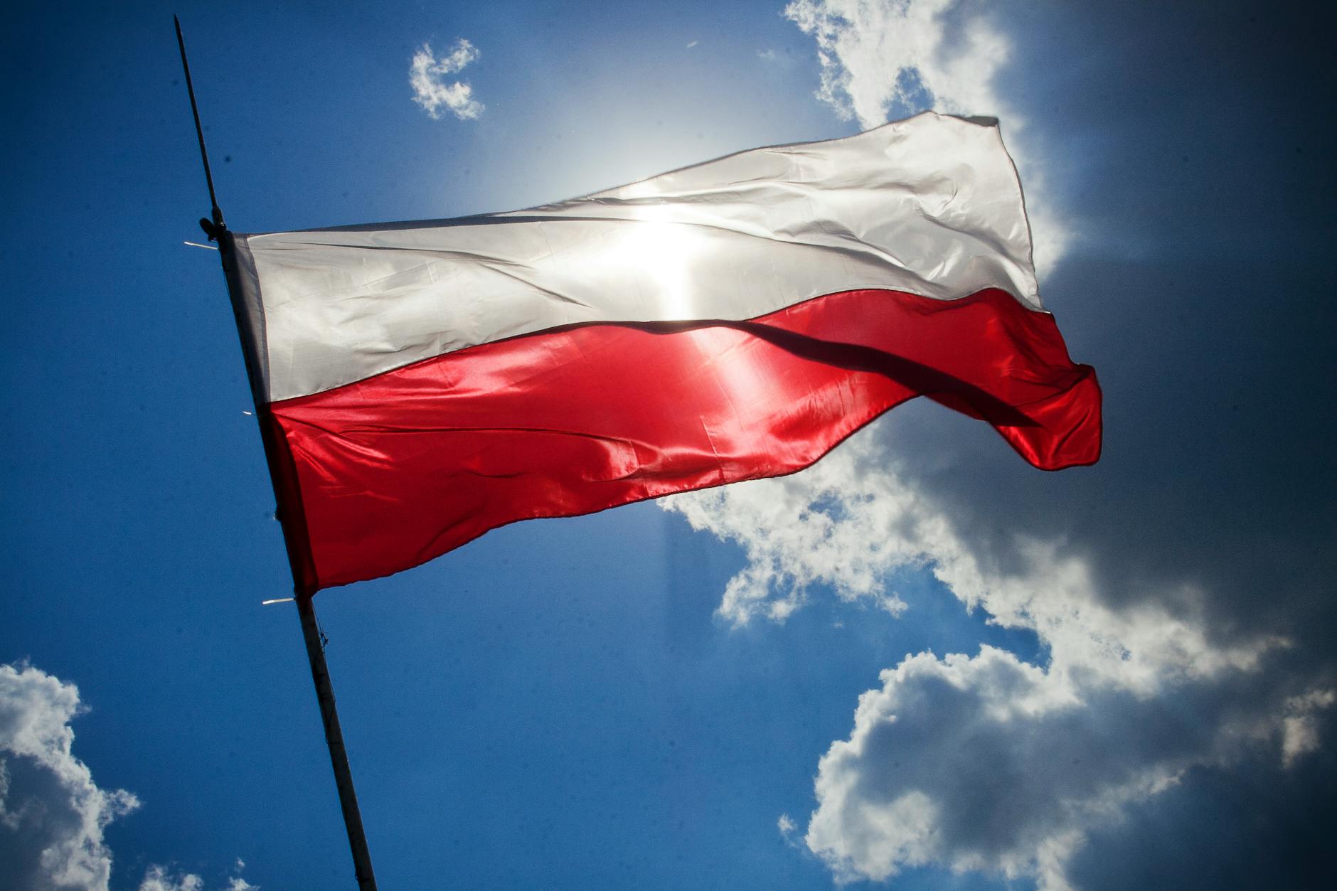 Powiewająca polska flaga na tle jasnego, niebieskiego nieba